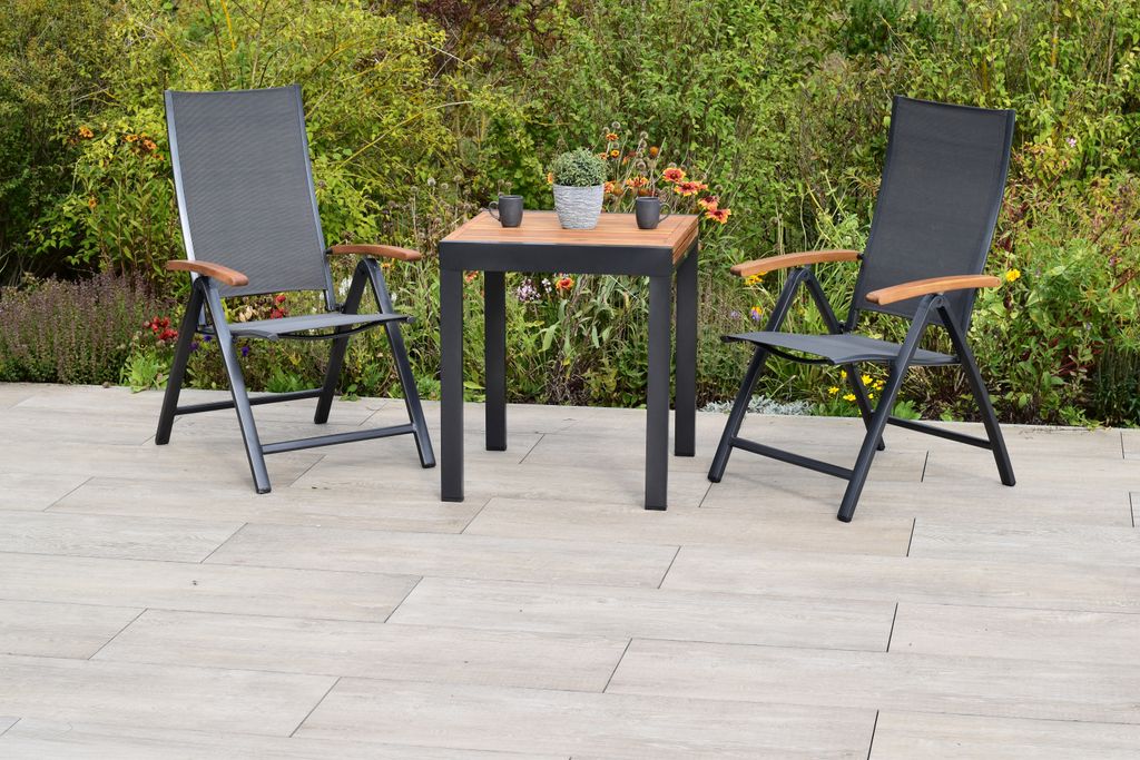 A patio set with two chairs and a table on a tiled patio, with greenery in the background.