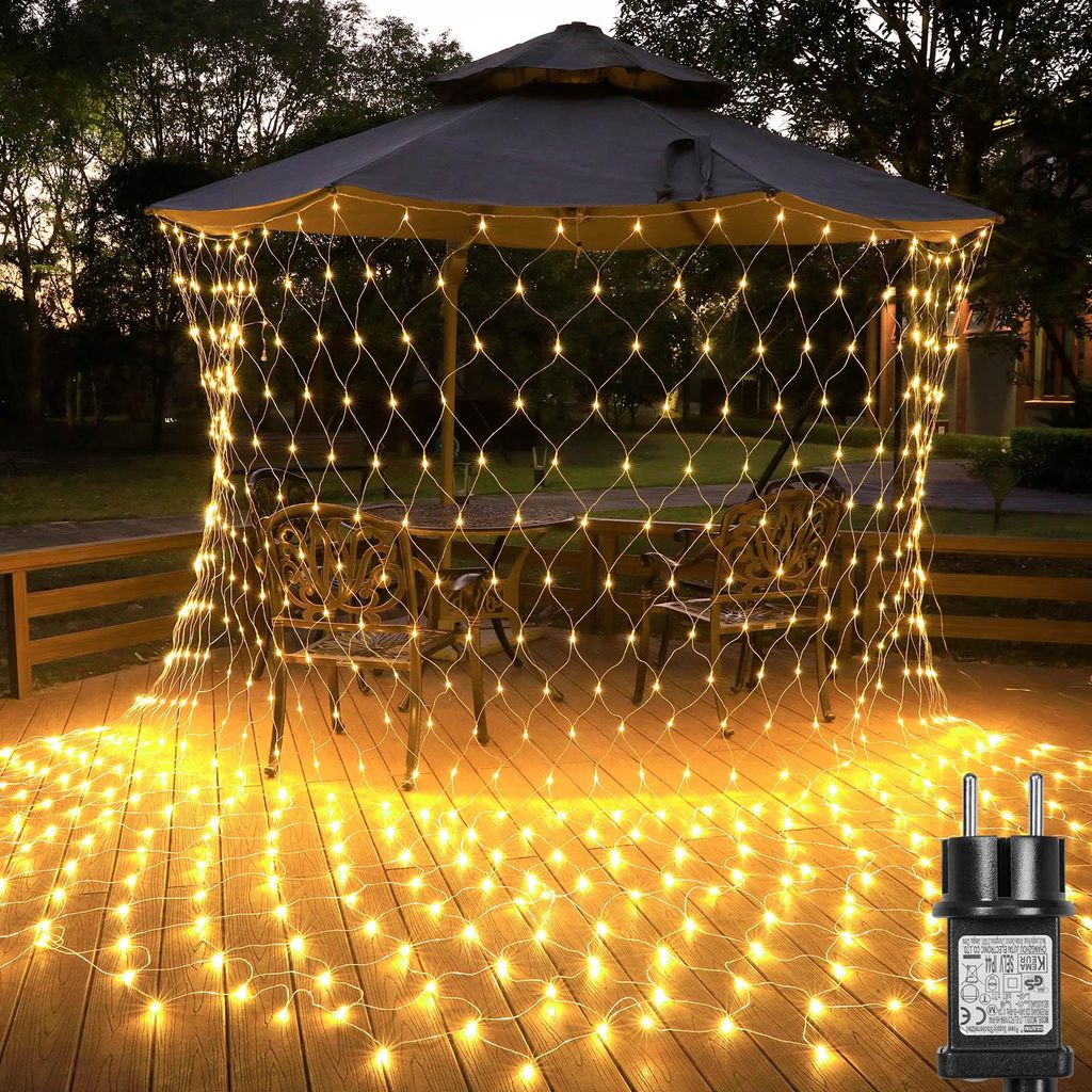 A net of fairy lights is draped over a gazebo and illuminates a wooden deck with chairs and a table.