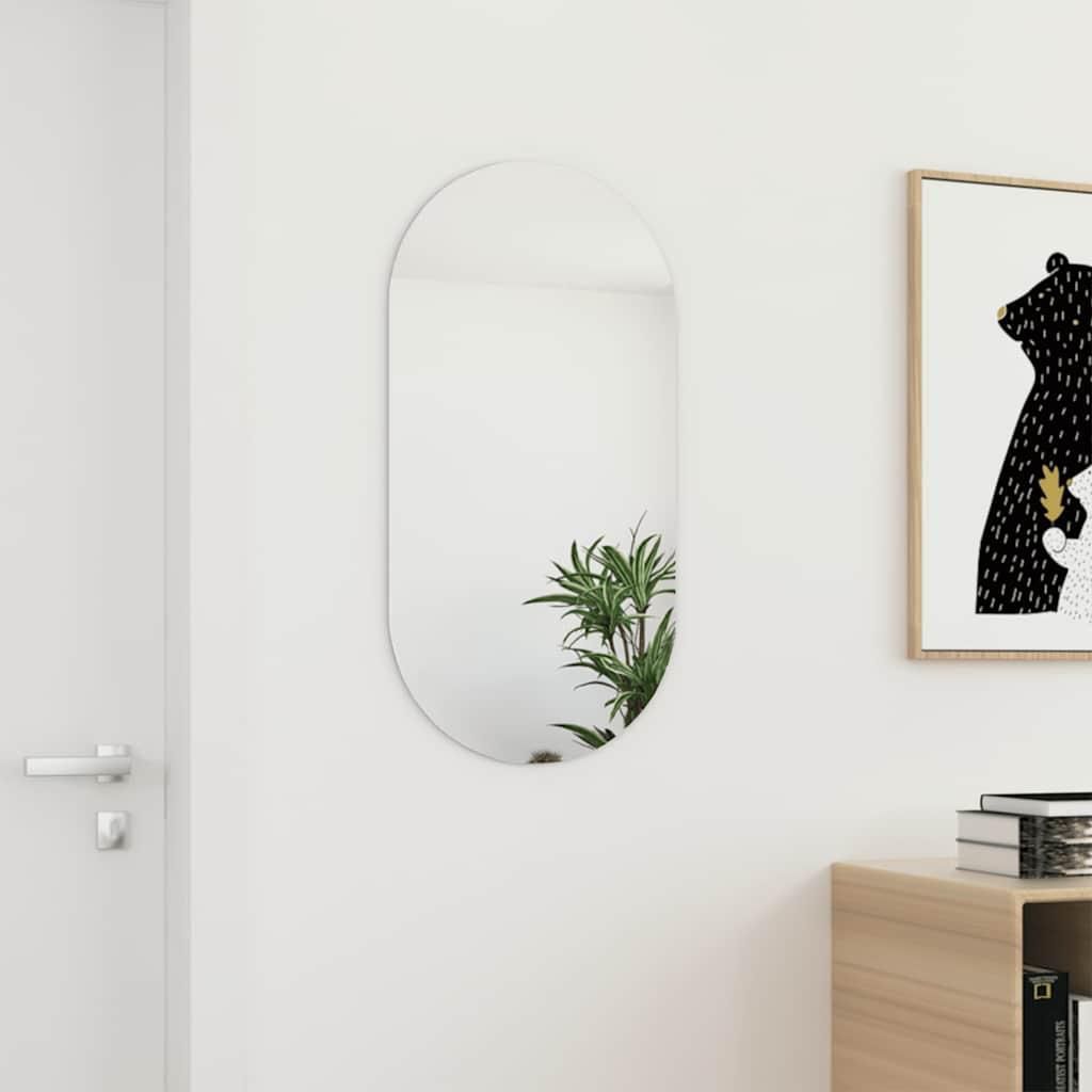 A modern oval mirror hangs on a white wall next to a door and a framed picture.