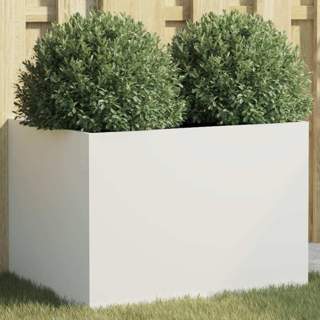 A white rectangular planter with two green bushes inside, placed on grass in front of a wooden fence.