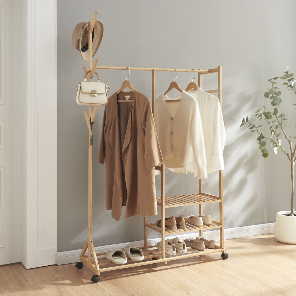 A wooden garment rack with clothes and shoes on it, placed in a room with a gray wall and wooden floor.