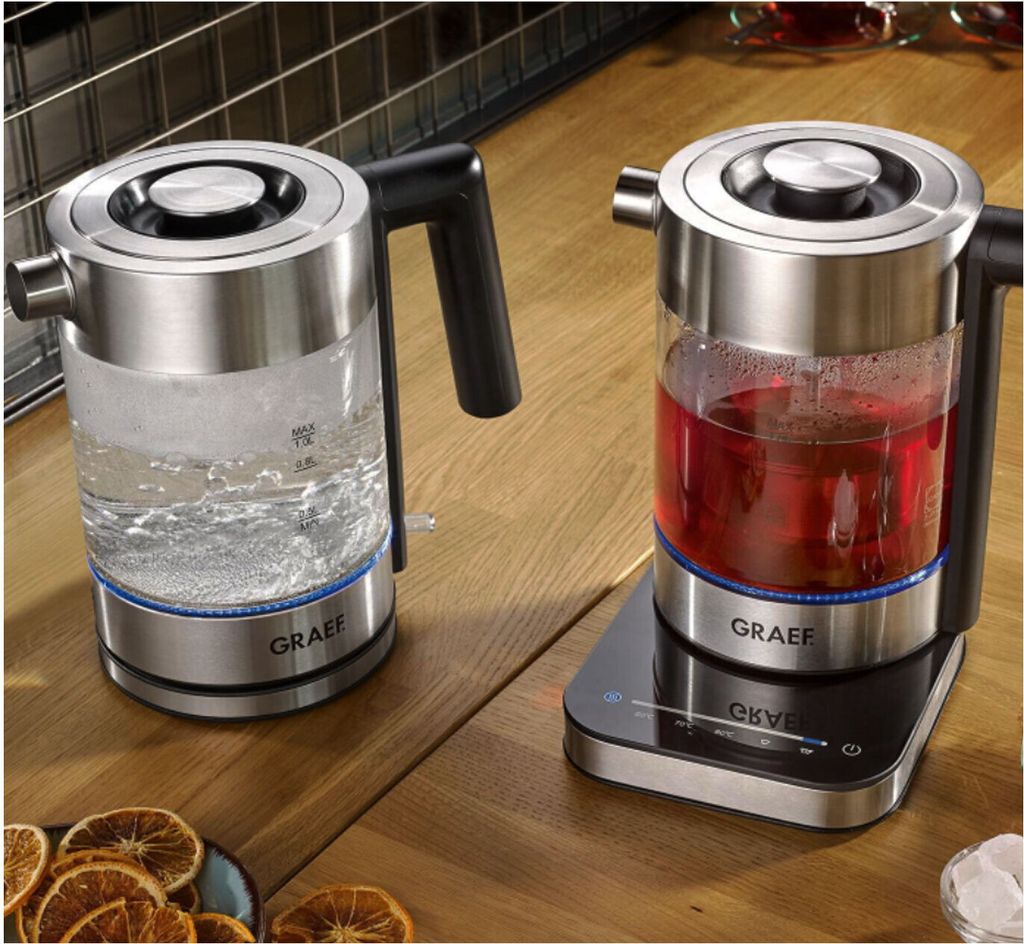 Two electric kettles on a wooden countertop, one filled with water and the other with red liquid.