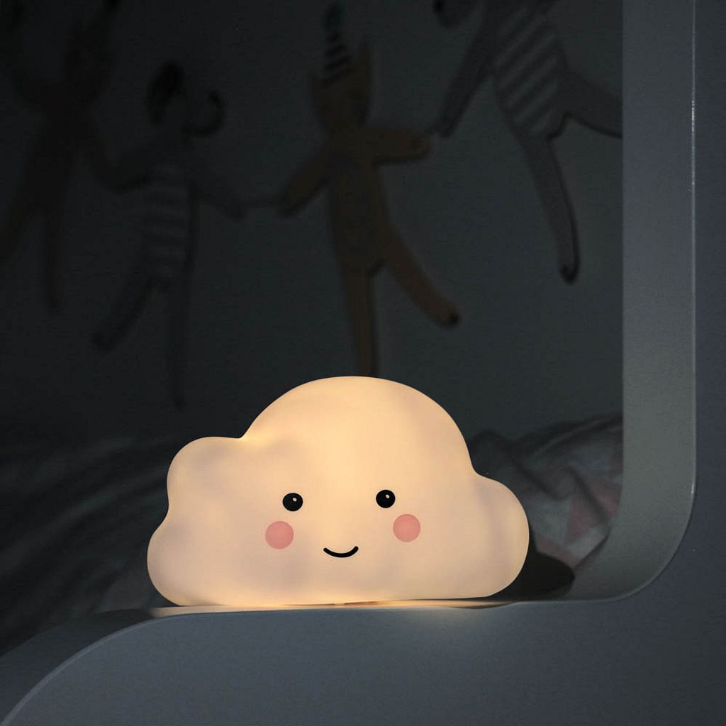 A cute cloud-shaped night light with a smiling face sits on a shelf in a dimly lit room.