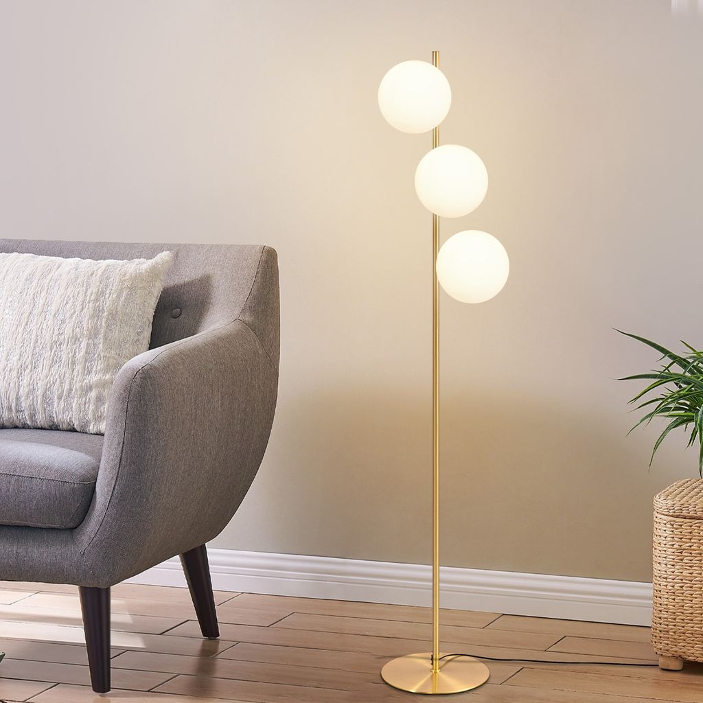 A modern floor lamp with three glass globes is placed next to a gray armchair in a living room.