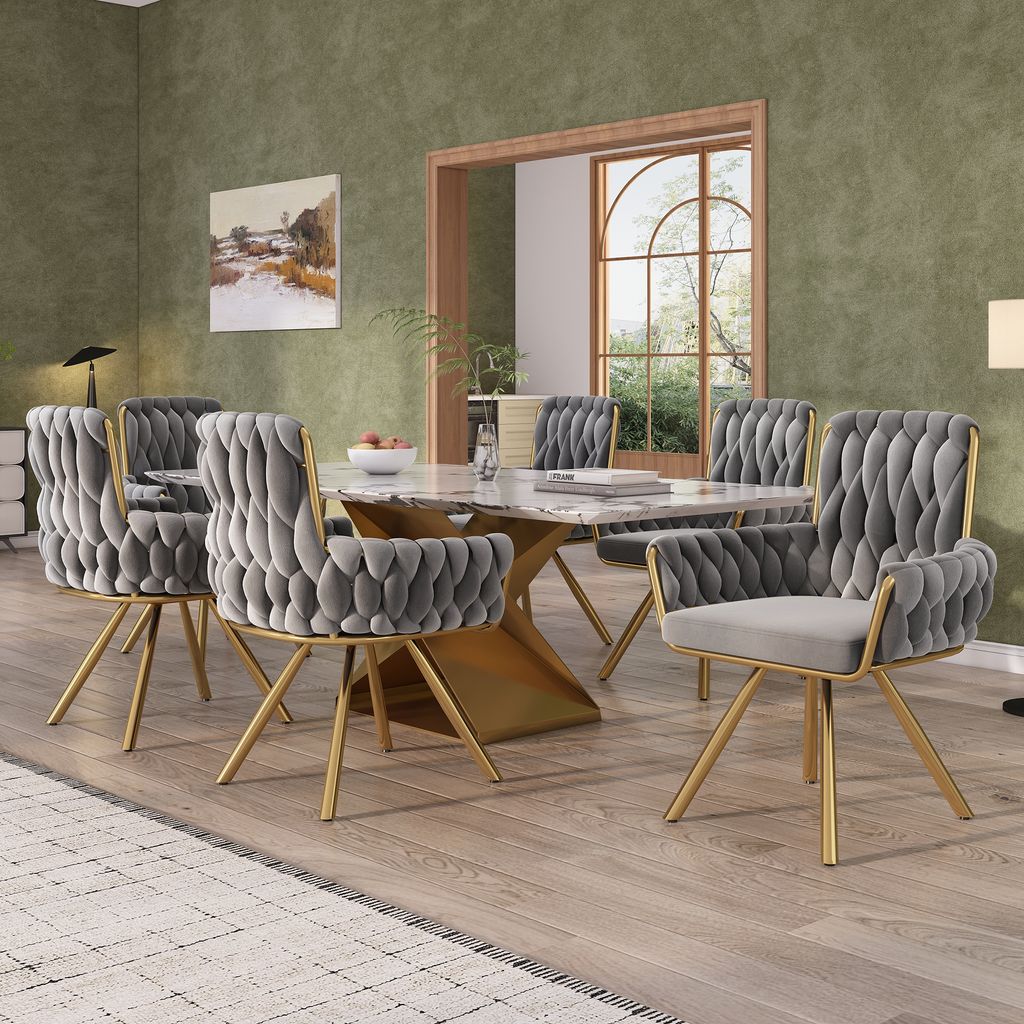 A dining room with a marble-topped table and six gray velvet chairs with gold legs.