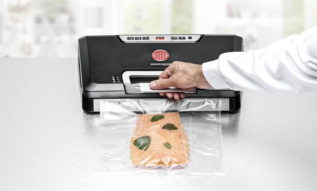 A hand is shown using a vacuum sealer to seal a piece of salmon in a plastic bag.