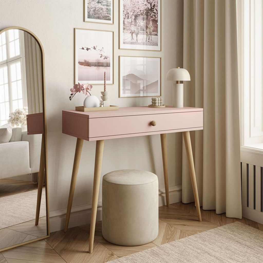 A pink console table with a wooden drawer knob and legs, a round beige stool, and several framed pictures on the wall.
