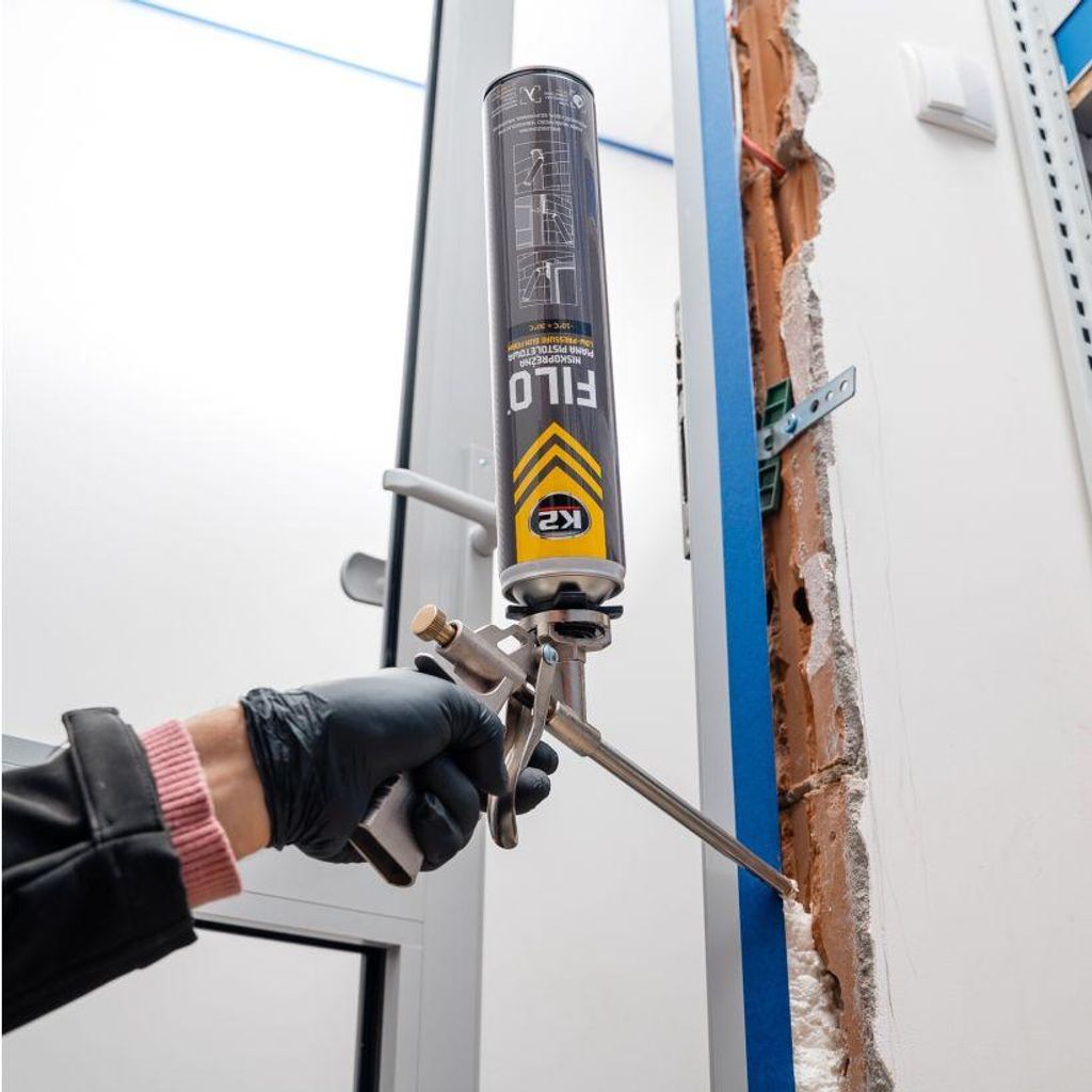 A person is using a can of spray foam to fill a gap in a wall next to a door frame.
