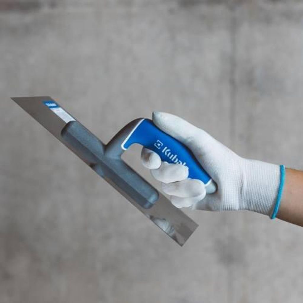 A hand wearing a white glove holds a trowel against a gray concrete wall.