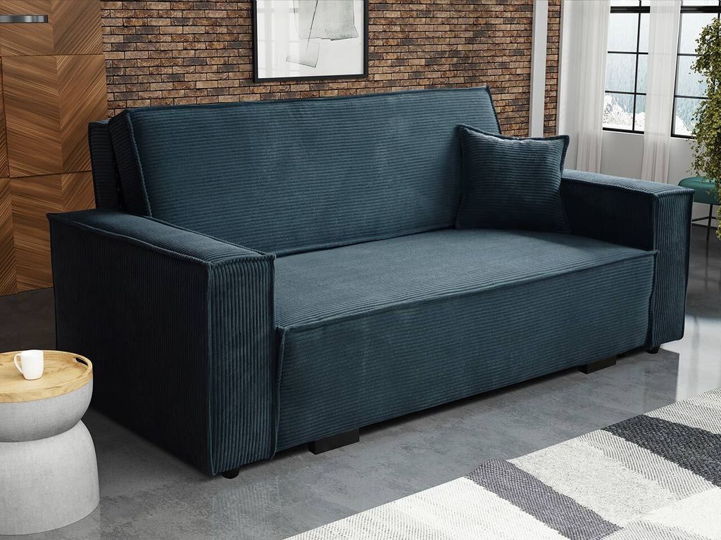 A blue corduroy sofa is shown in a room with a brick wall and a rug.