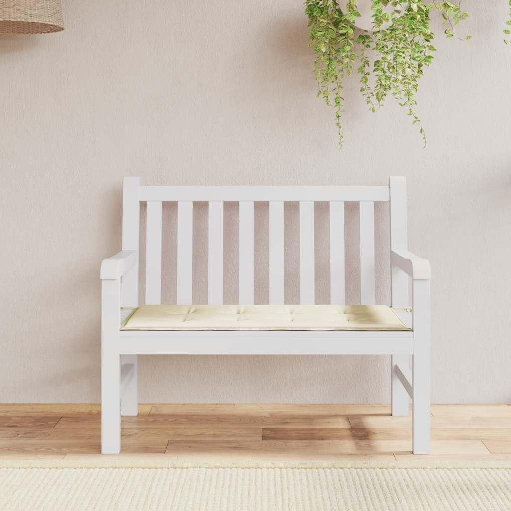 A white garden bench with a cream cushion, placed on a wooden floor in front of a light pink wall with hanging plants.