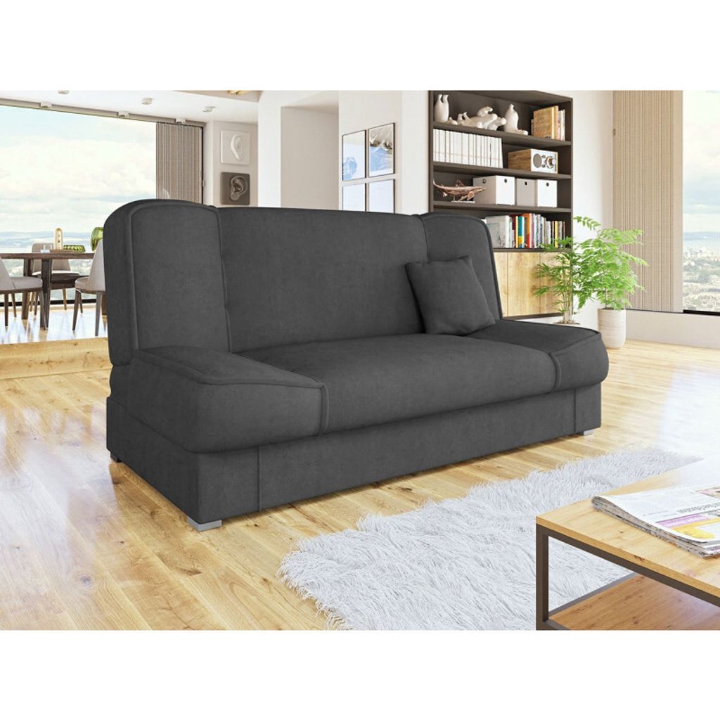 A dark gray sofa in a modern living room with a wooden floor, white rug, and a coffee table with magazines.