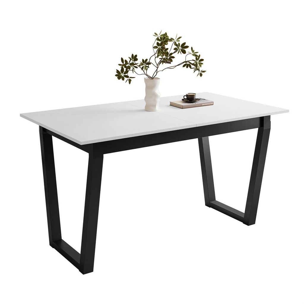 A white tabletop with black V-shaped legs, decorated with a vase of green leaves and a small book with a cup on top.