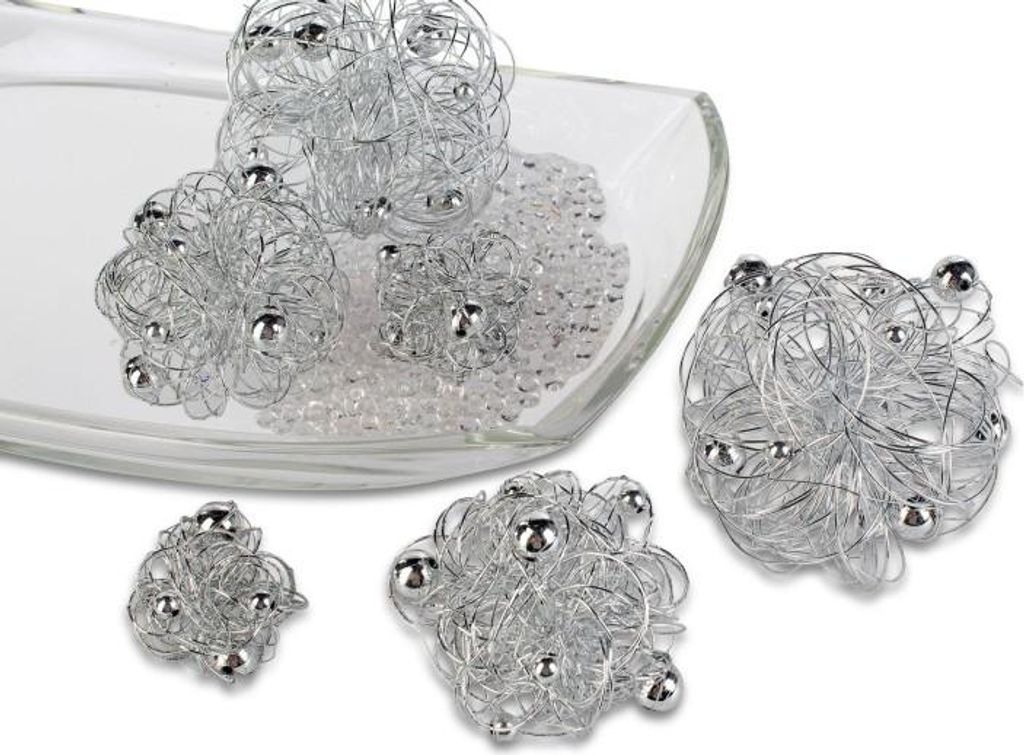 Several decorative wire balls with silver beads are arranged on a clear glass dish filled with small clear beads, with some balls outside the dish.