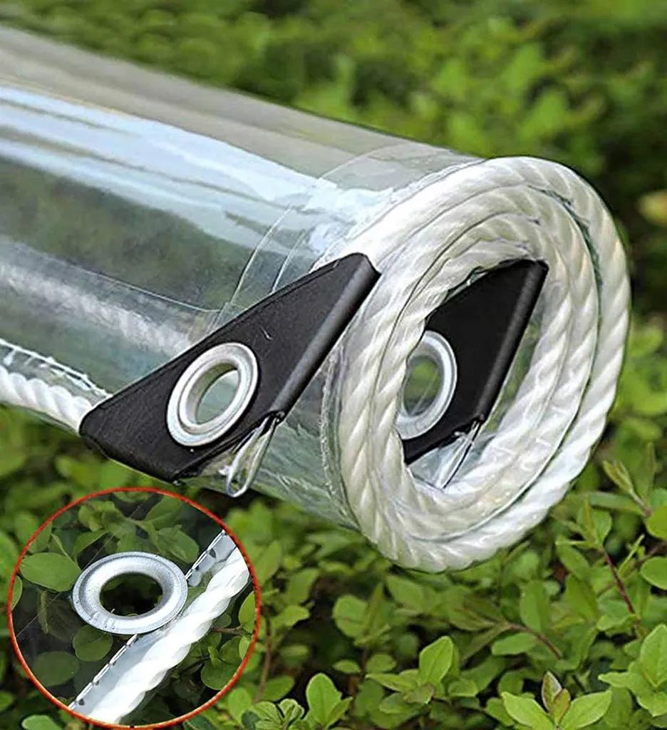 A close-up of a rolled-up clear tarp with rope and grommets, resting on green foliage.