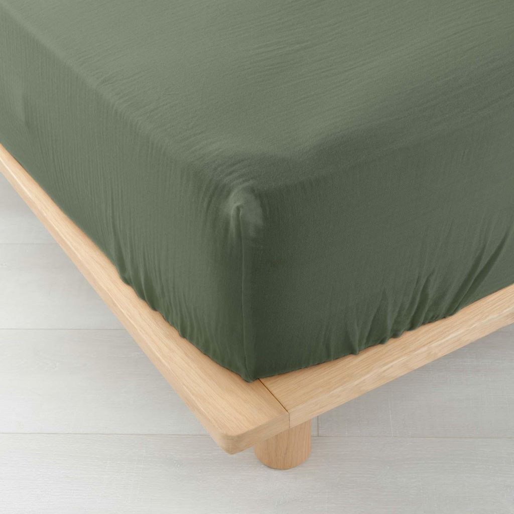 A close-up view of a green fitted sheet on a wooden bed frame.