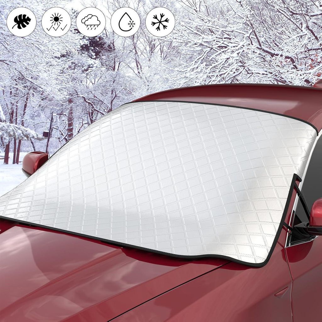 A car windshield cover is placed on a red car in a snowy environment.