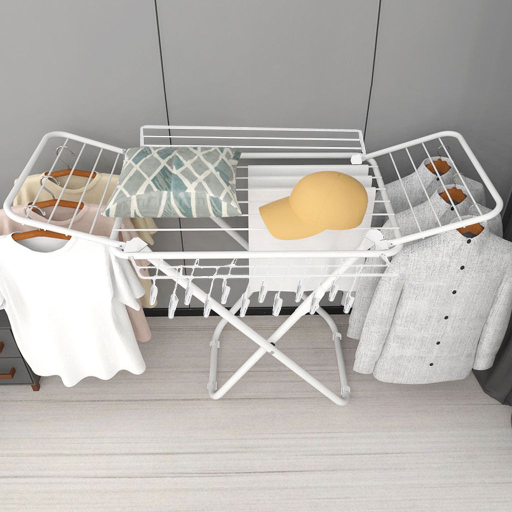 A white folding drying rack with clothes and accessories on it, set against a light gray wall and a light wooden floor.