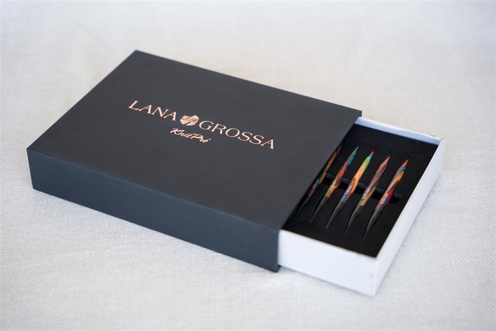 A dark gray box with the Lana Grossa logo and text is partially open, revealing a set of colorful knitting needles inside.