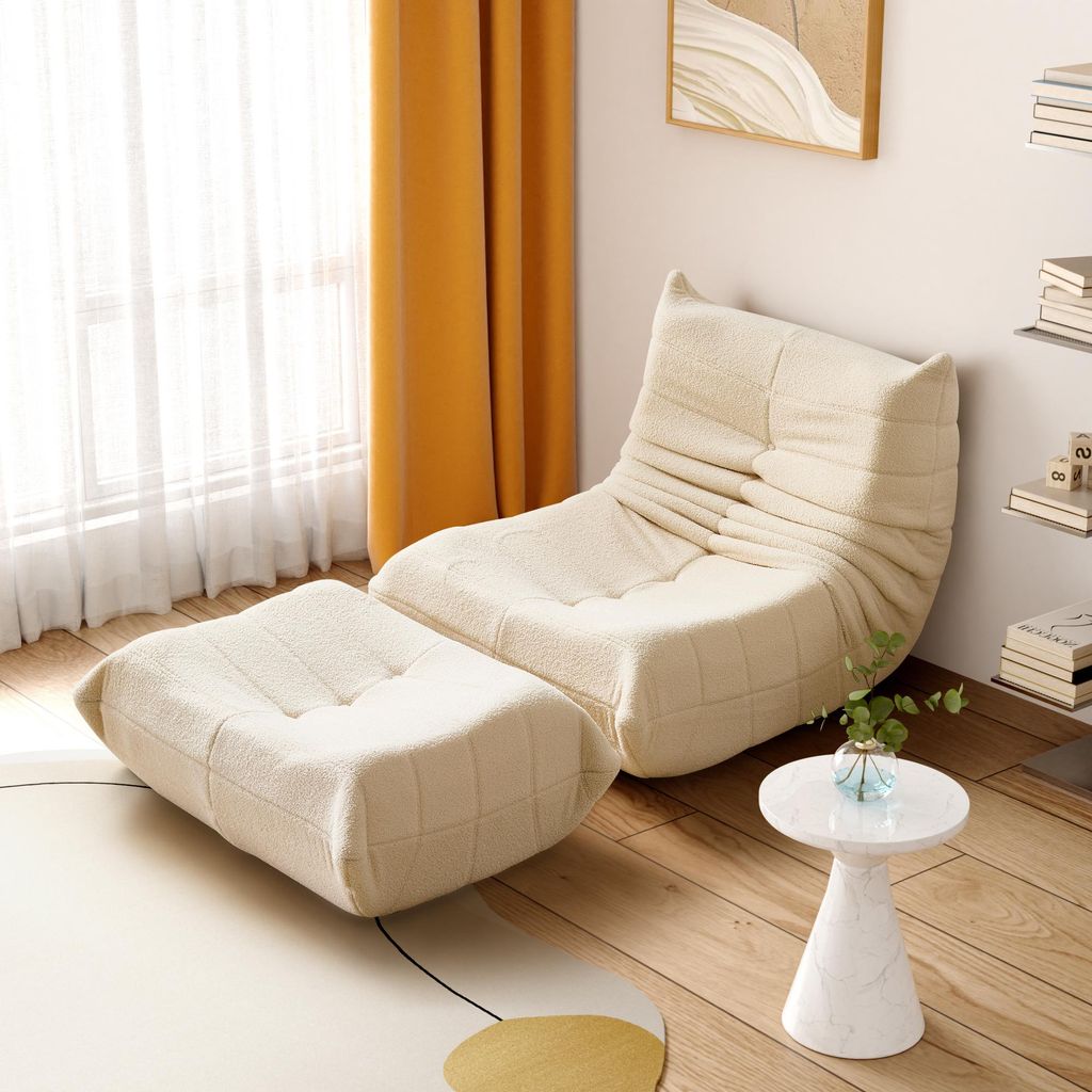 A beige armchair and ottoman are placed in a room with yellow curtains and a small white side table.