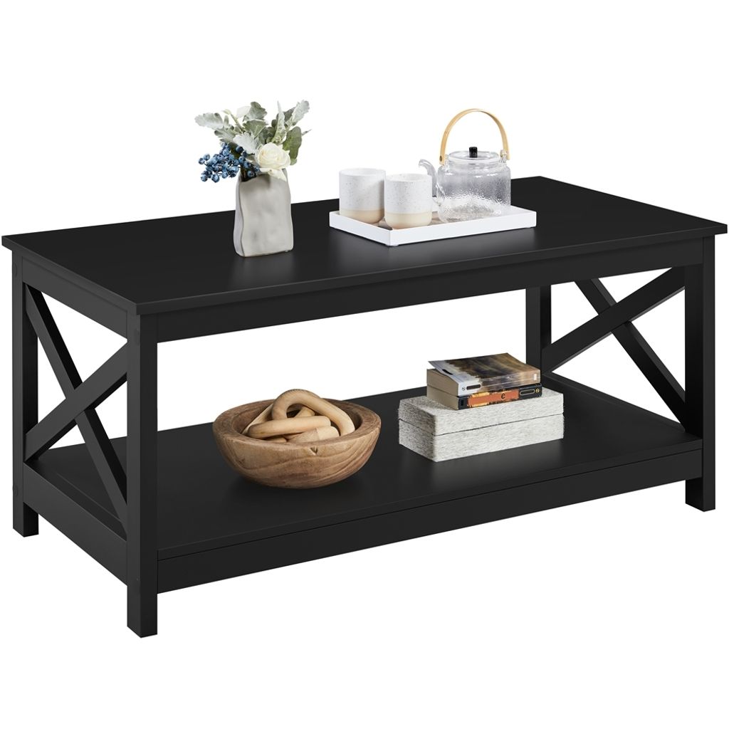 A black coffee table with a lower shelf, decorated with a vase of flowers, teacups, a teapot, a wooden bowl with decorative items, and books.