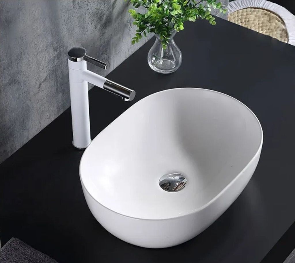 A white oval countertop sink with a white faucet on a black countertop.