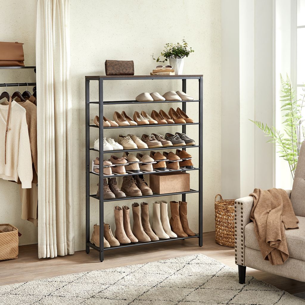 A multi-tiered shoe rack filled with various shoes, along with some clothing items hanging on a rack to the left and a chair to the right.