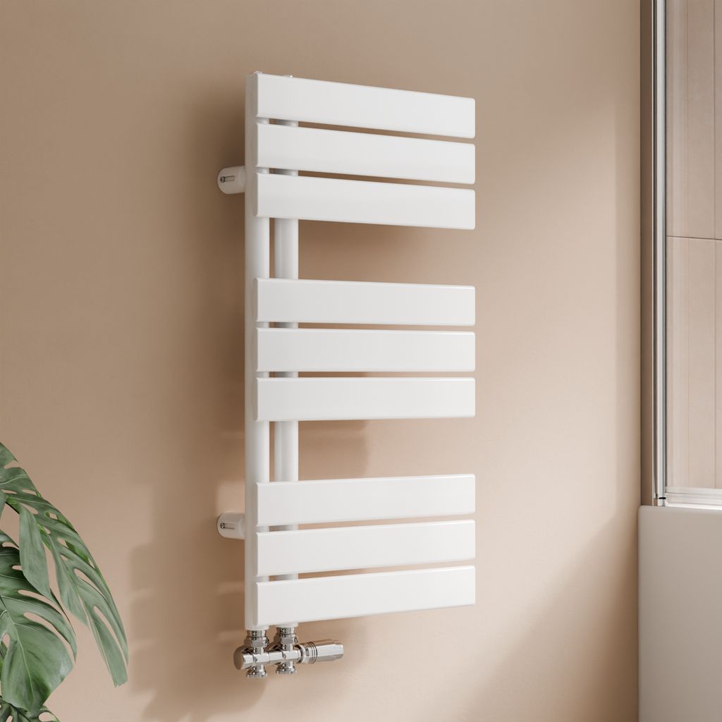 A white designer radiator mounted on a beige wall, with a plant in the foreground and a shower enclosure in the background.