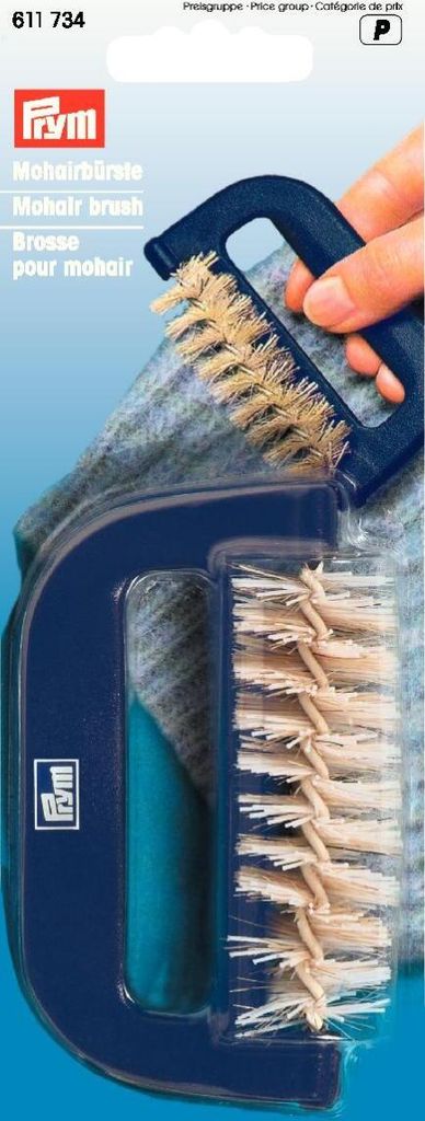 A hand is holding a blue mohair brush over a piece of grey fabric.