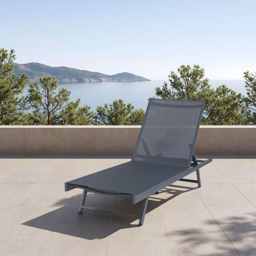 A dark gray chaise lounge is positioned on a tiled patio overlooking a body of water and distant hills.