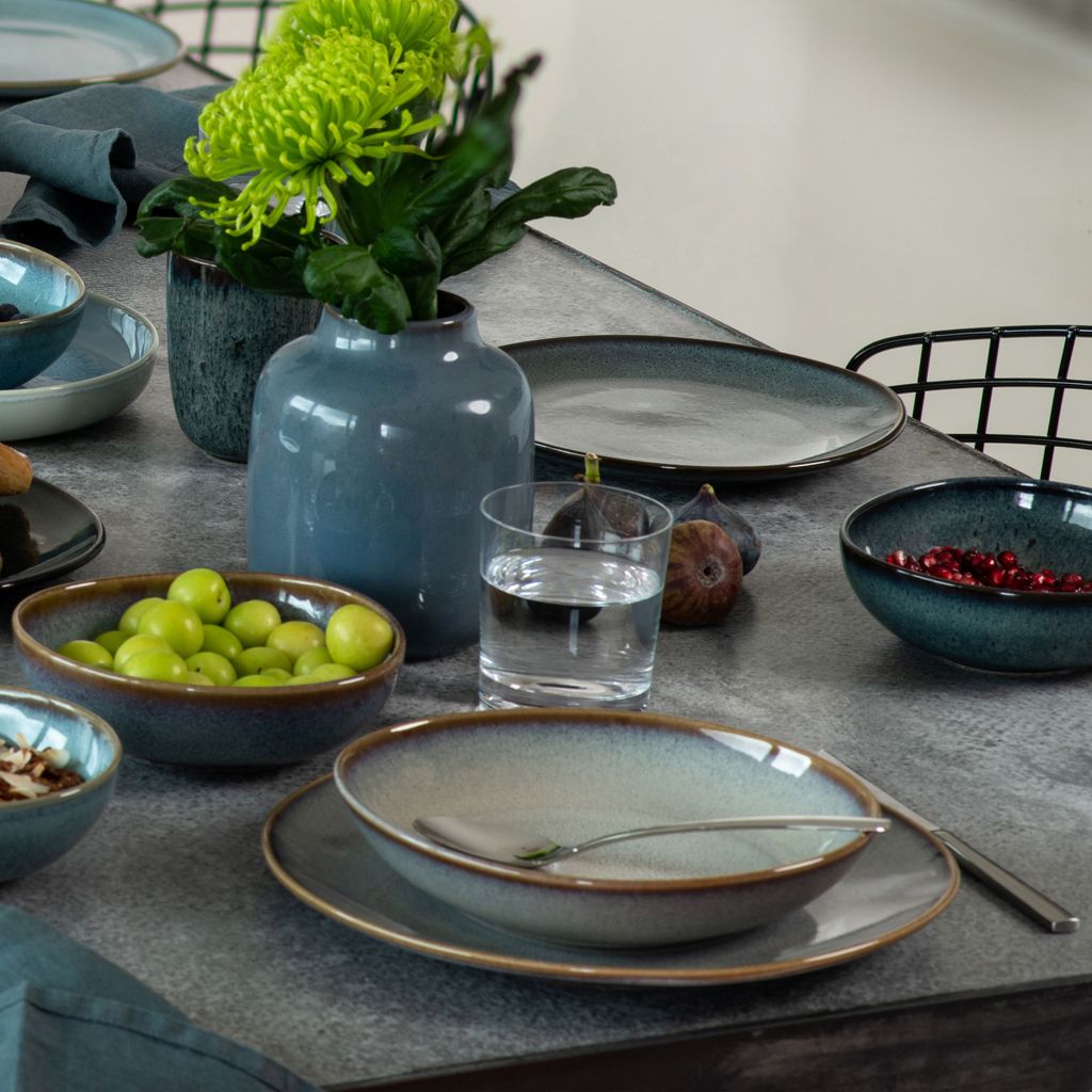 A table setting with plates, bowls, fruit, and a vase of flowers.