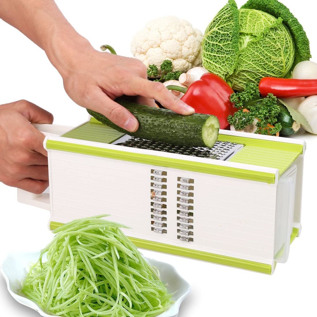 A hand is using a multi-functional grater to shred a cucumber, with a pile of shredded cucumber in a bowl in the foreground and various vegetables in the background.