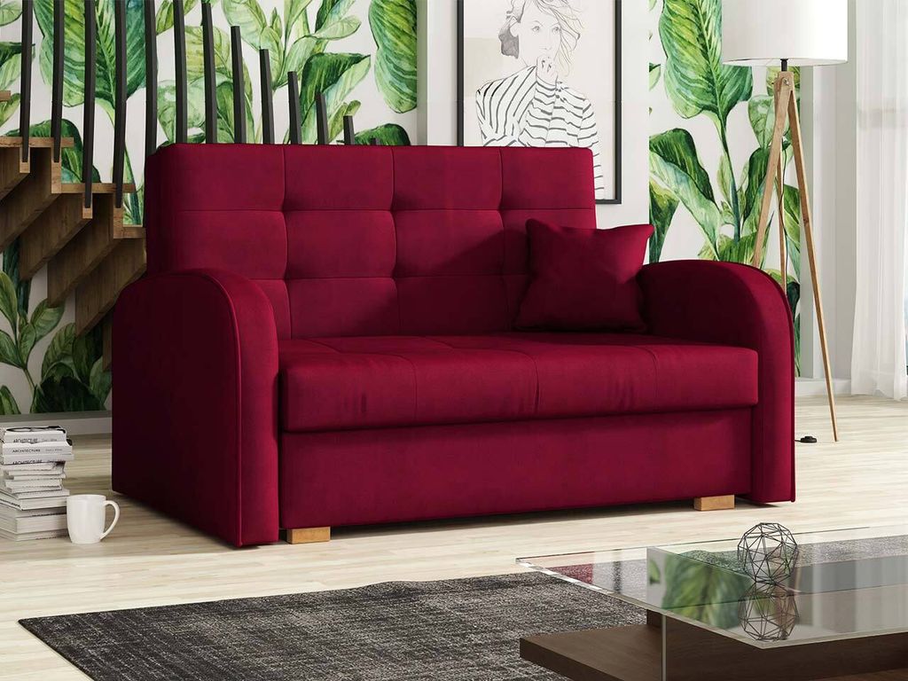 A red sofa bed is shown in a living room setting with a staircase and a floor lamp in the background.