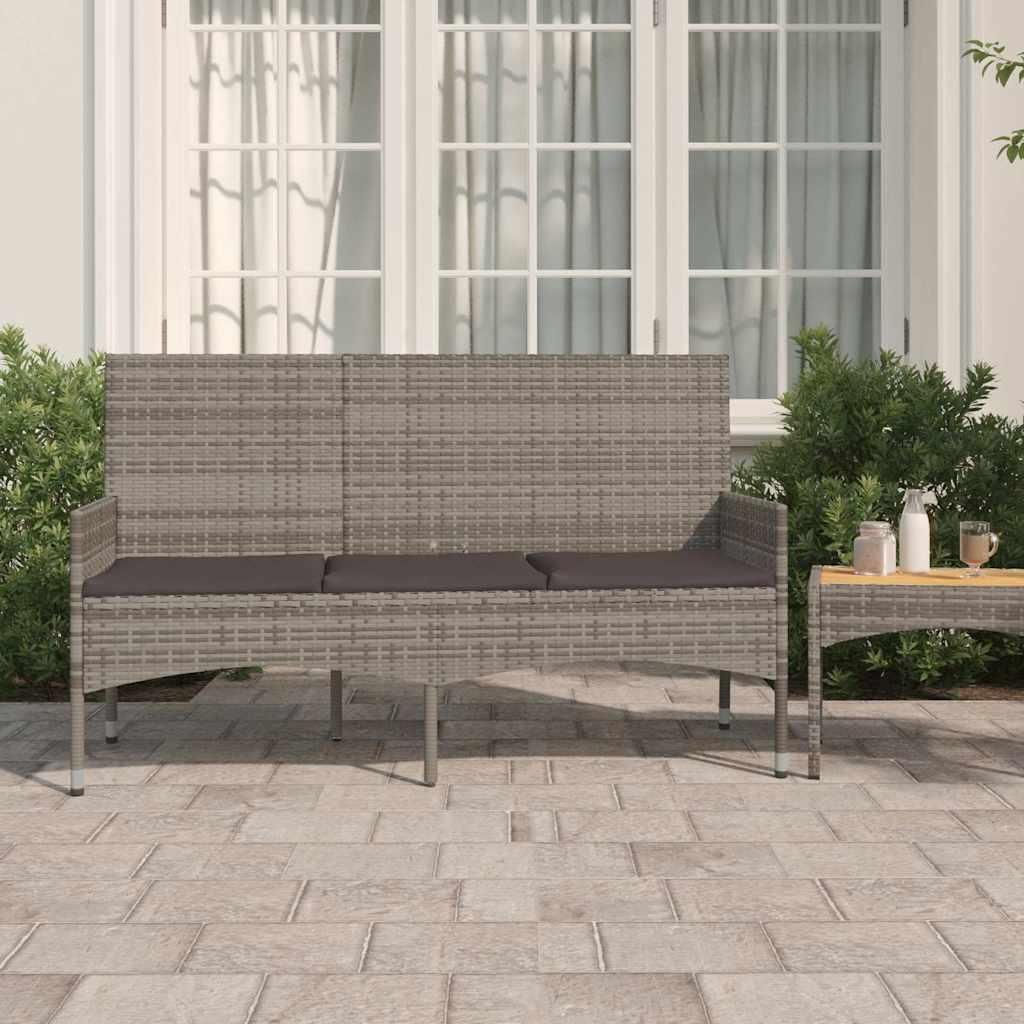 A three-seater garden bench with cushions on a paved patio in front of a building with large windows.