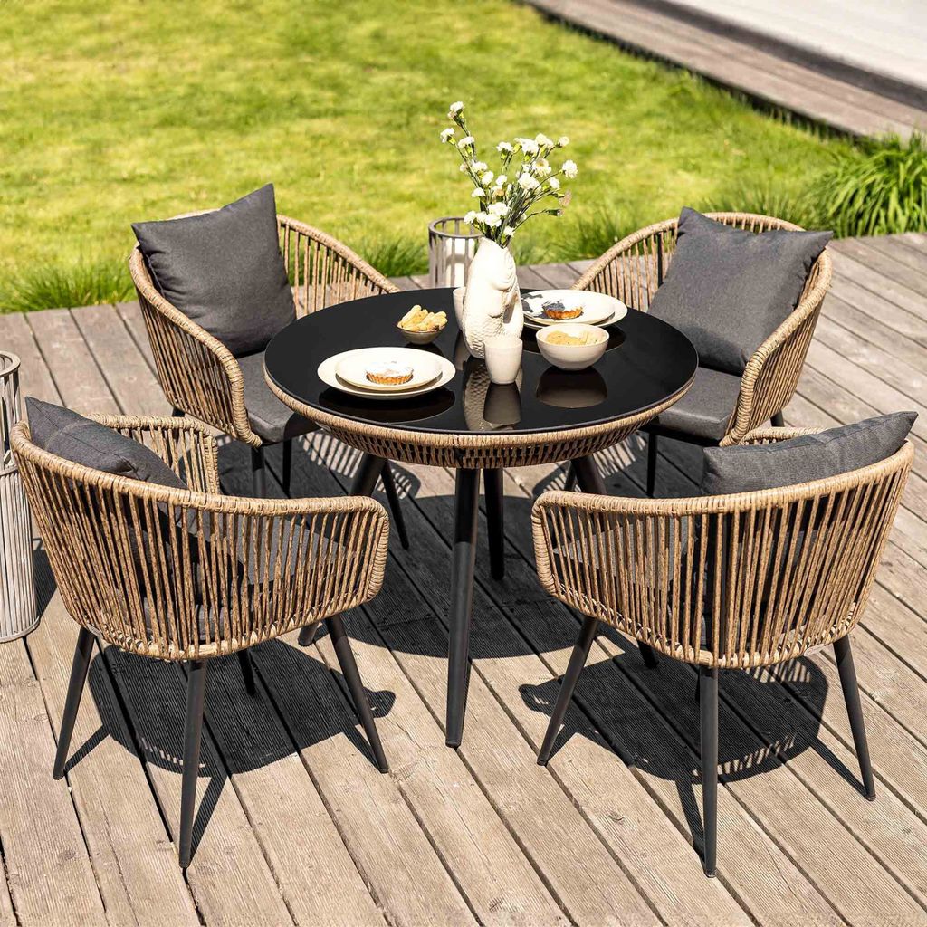A four-person outdoor dining set with a round table and four chairs on a wooden deck, with a grassy area in the background.