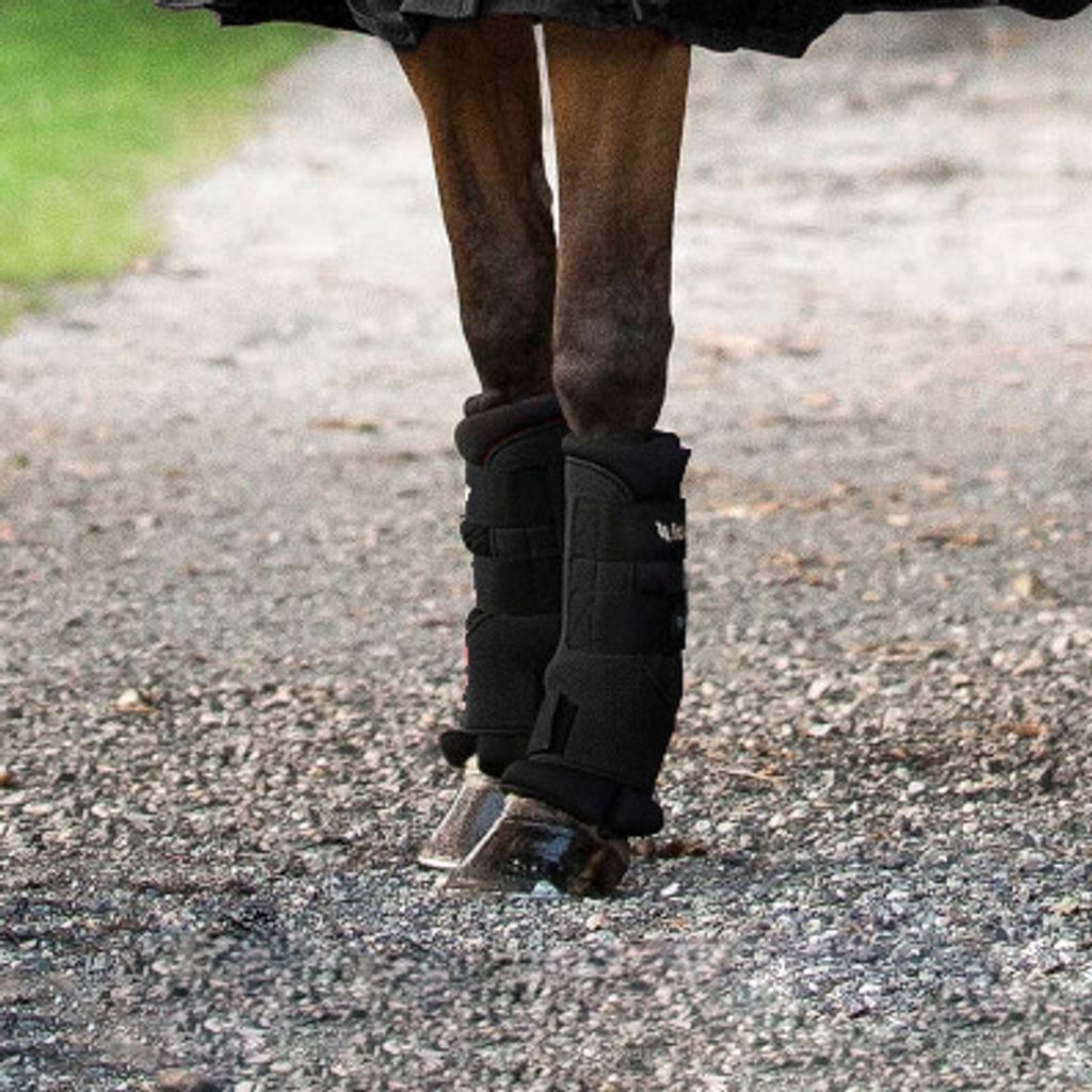 Close-up of a horse's legs wearing black stall boots, standing on a gravel path.