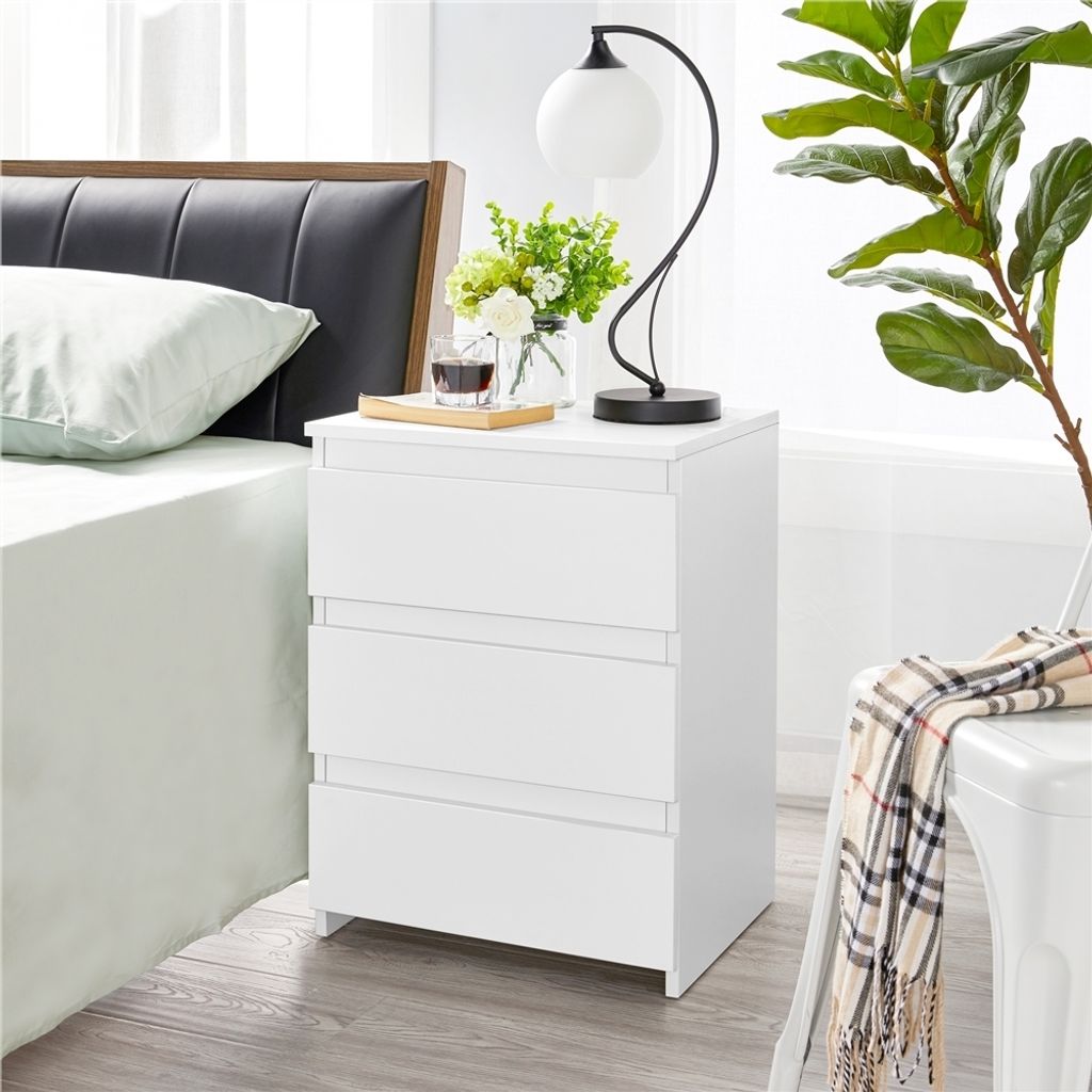 A bedside table with a lamp, flowers, and a drink next to a bed.
