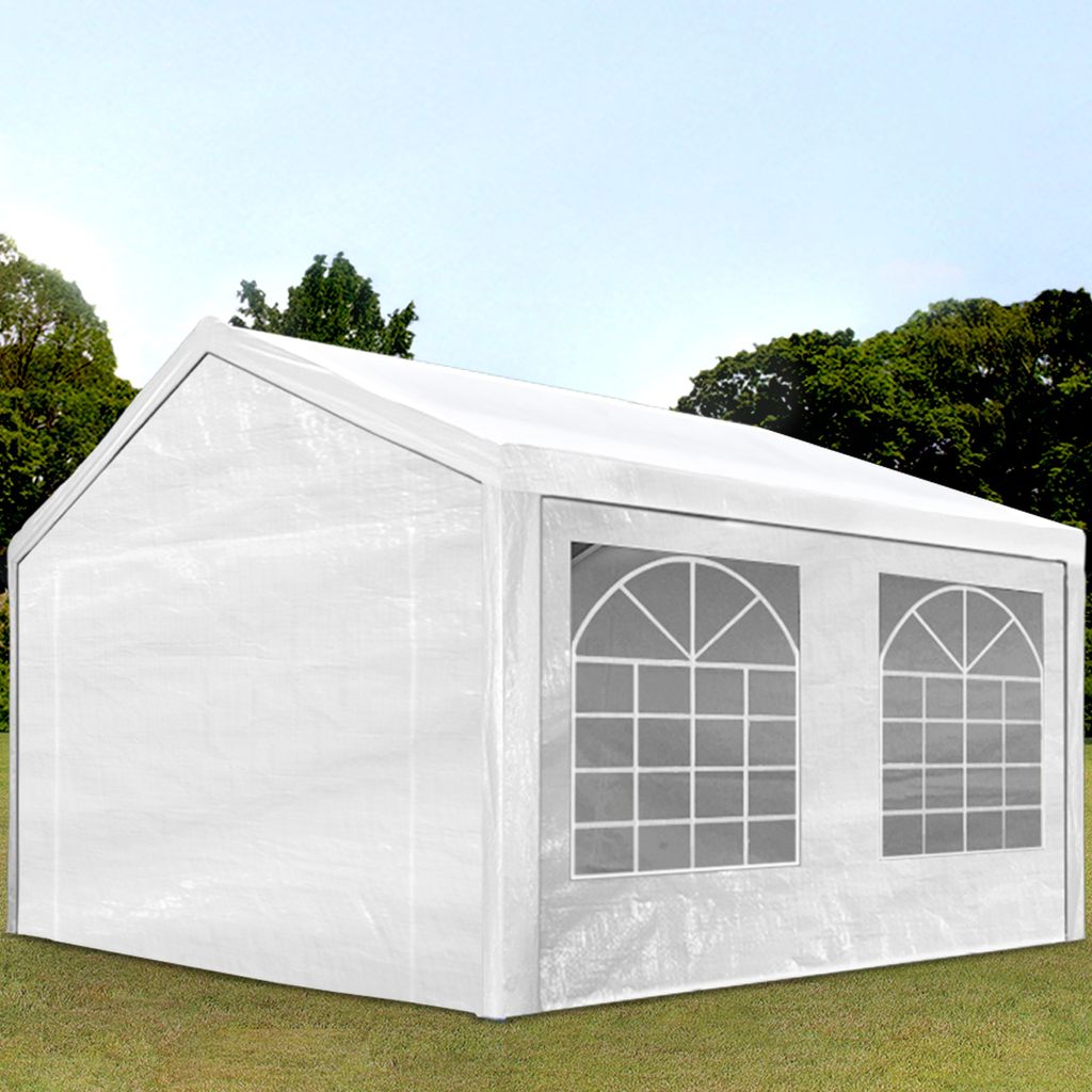 A white party tent with arched windows is set up on a grassy lawn with trees and a blue sky in the background.