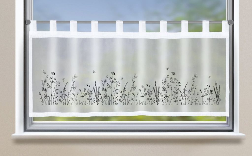 A sheer cafe curtain with a floral design is shown hanging in a window.