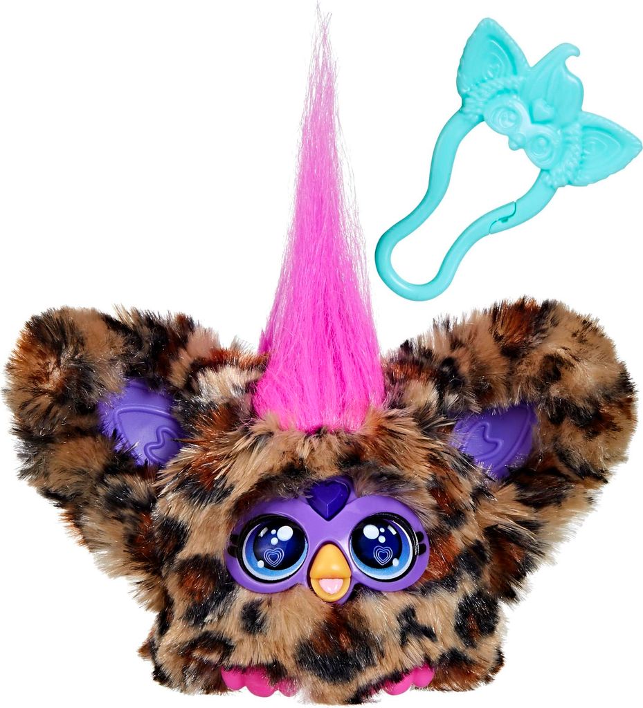 A close-up studio shot of a Furby Furblet toy with a leopard print pattern, bright pink hair, and large blue eyes. A teal accessory with ear-like shapes is positioned above and to the right of the toy.