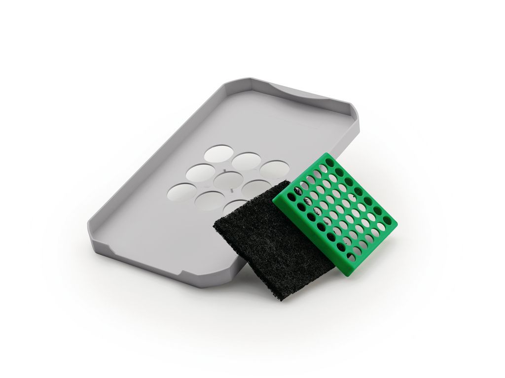 A light gray plastic tray with circular cutouts, a black filter, and a green perforated plastic grid are arranged on a white background.