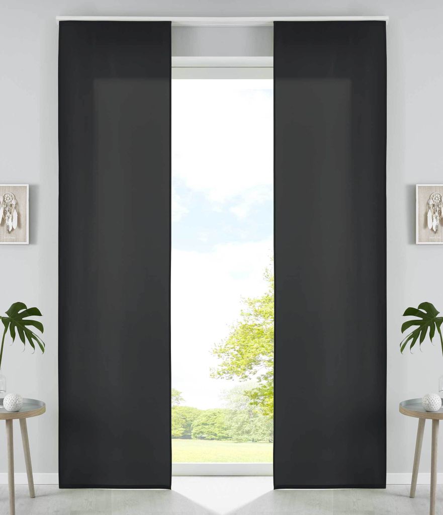 Two dark gray panel curtains are drawn, partially obscuring a window with a view of trees and sky. Small decorative items and plants are visible on either side of the window.