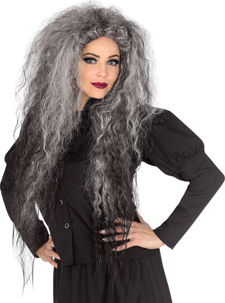 A woman wearing a black dress and a long, wild, gray and black wig, posing with her hands on her hips.