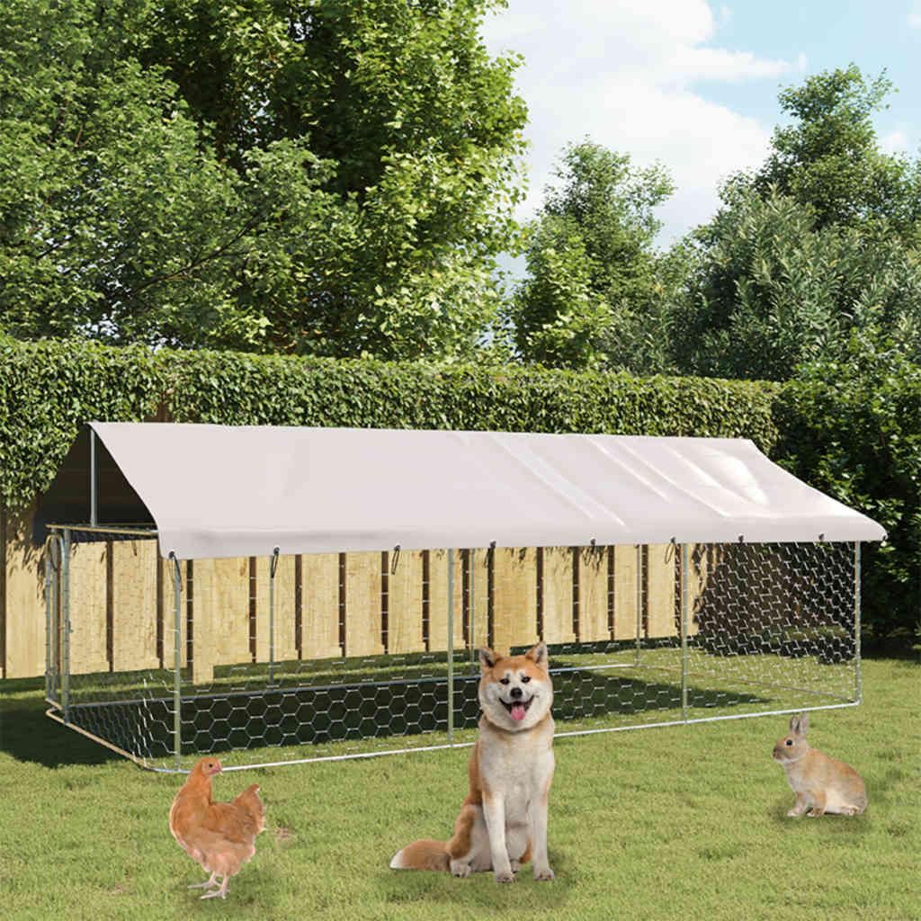 A large outdoor dog kennel with a white roof, set up in a grassy yard with trees and a fence in the background. A dog, a chicken, and a rabbit are in front of the kennel.