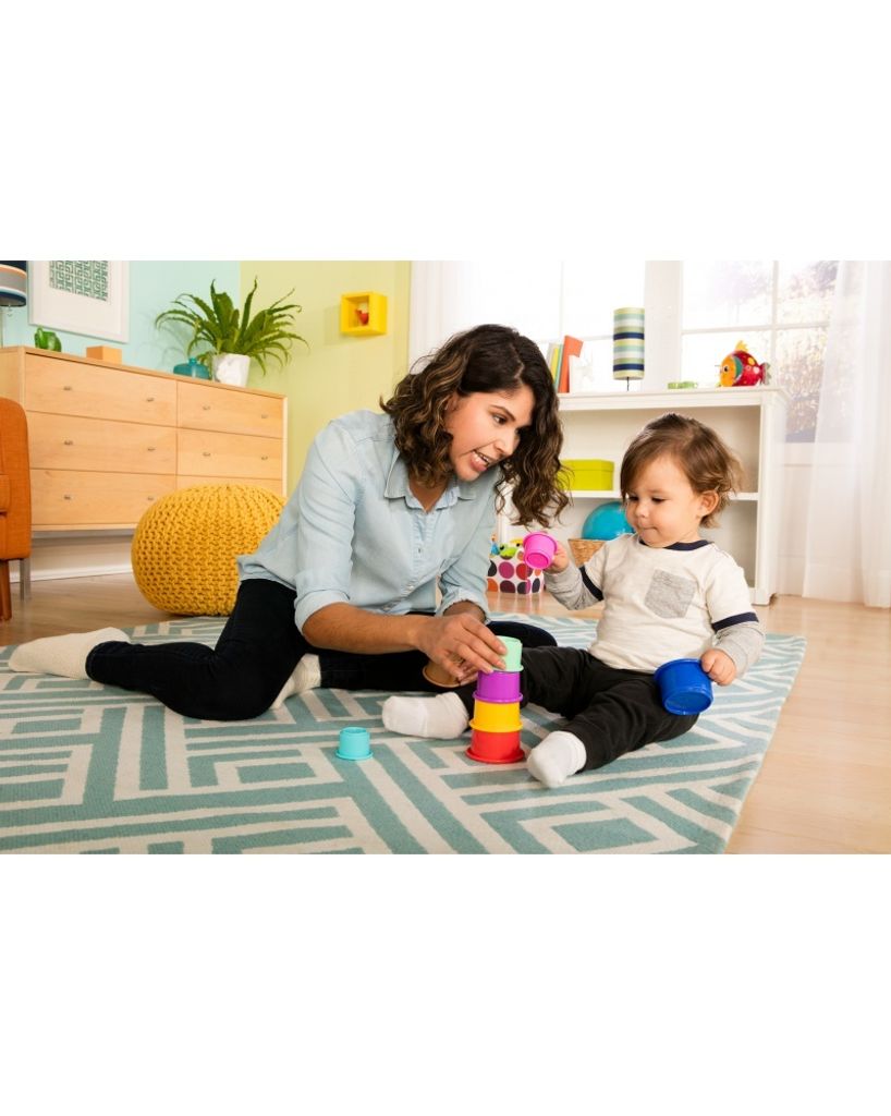 A woman and a baby are playing with stacking cups on a rug.