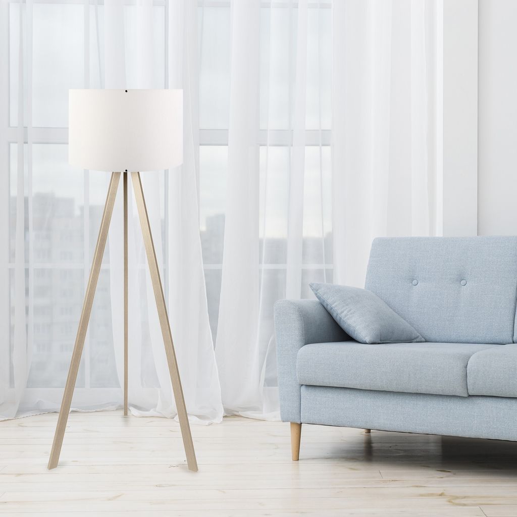 A floor lamp and a sofa are in a room with sheer white curtains in the background.