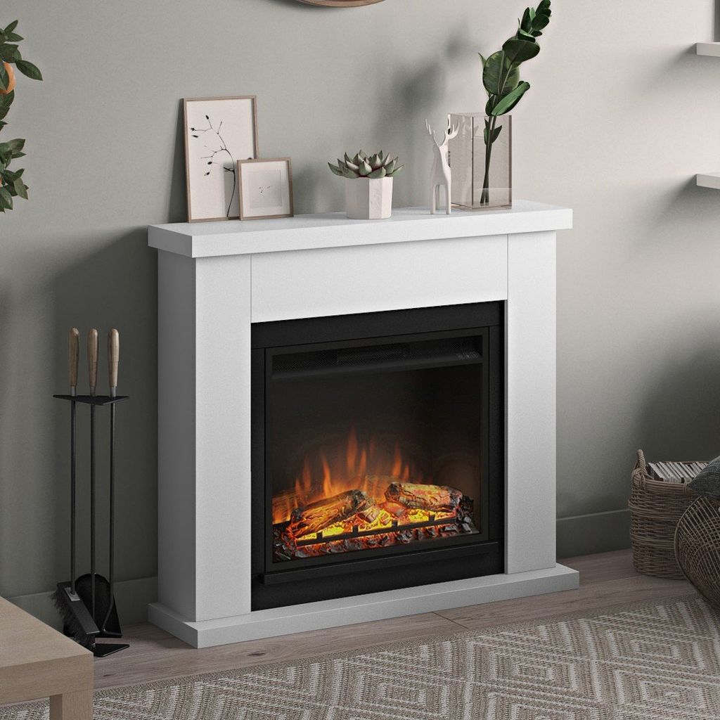 A white electric fireplace with a realistic flame effect, set in a living room with decorative items on top and a fireplace tool set beside it.