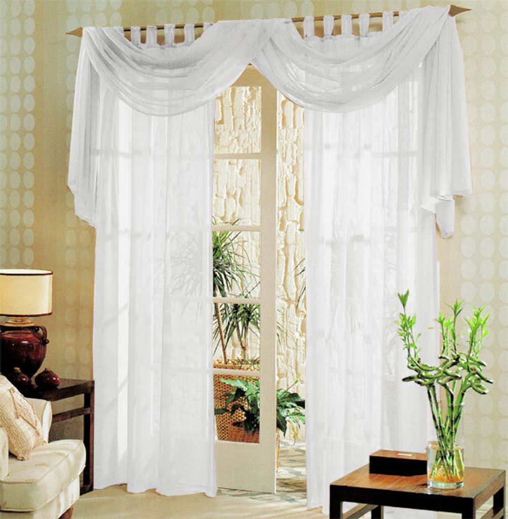 A set of white voile curtains draped over a doorway, with a glimpse of plants and a stone wall visible through the doorway.