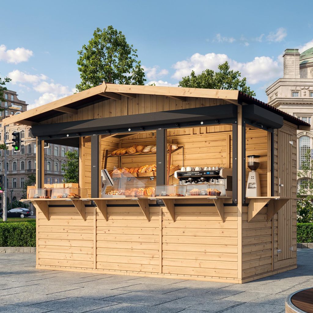 A wooden market stall selling baked goods and coffee, set up outdoors in a paved area with buildings and trees in the background.