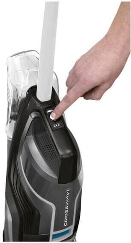 A hand is pressing a button on a black and gray Bissell CrossWave C6 3569N Select cordless vacuum cleaner.